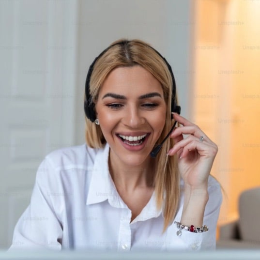 A smiling woman wearing a headset while working on a computer.