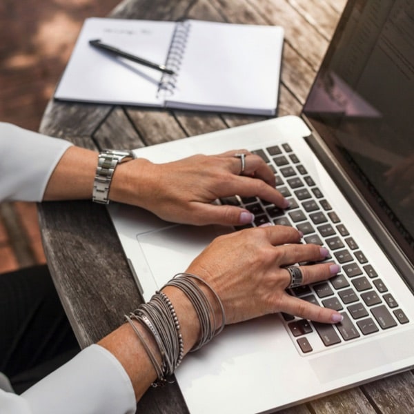 A woman typing on a laptop on a wooden table.
